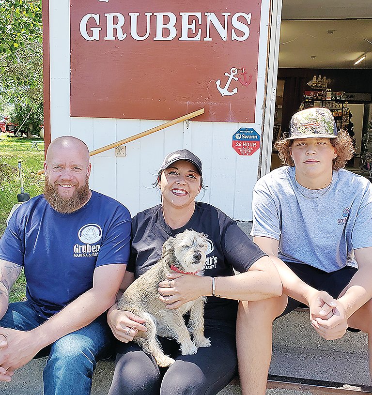The new owners 
of Gruben’s Marina and Resort on the steps outside the business’s general store. Pictured are Fred Brett, Chessica Reichert, and their son Jace.