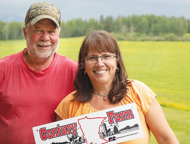 Standing on the deck of their home overlooking the fields and trees below, Craig and Valarie Flank display the Century Farm sign from the Minnesota State Fair and Minnesota Farm Bureau.