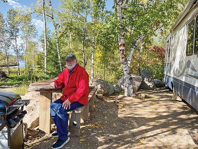 Dave Rose sits at a makeshift picnic table at one of the RV lots, where a new owner has already parked an RV.  Final landscaping is still needed but the project is now close to completion. photo by M. Helmberger