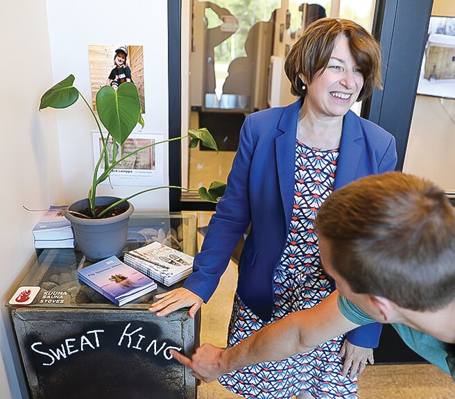 Sen. Amy Klobuchar smiles as Garrett Lamppa points out the lettering on one of the company’s original sauna stoves, which sits in the lobby at the company’s new manufacturing plant.