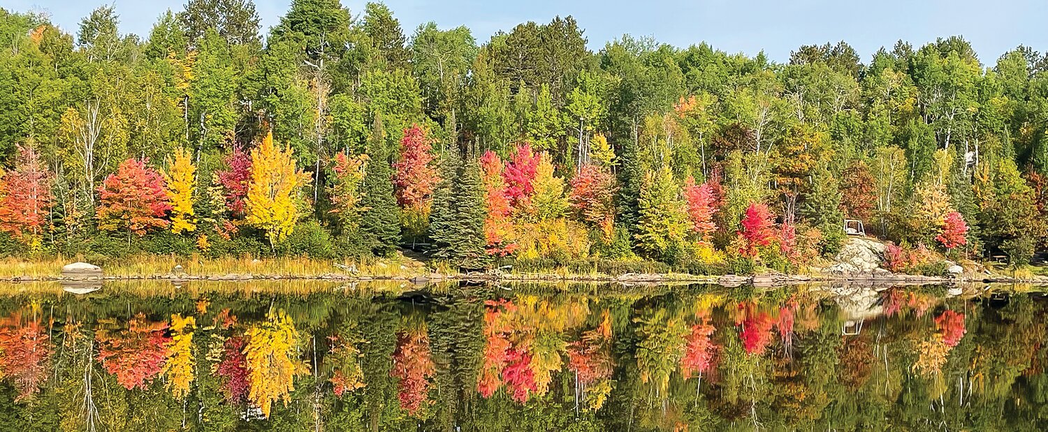 A colorful shoreline along the Pike River Flowage is reflected on still morning water.