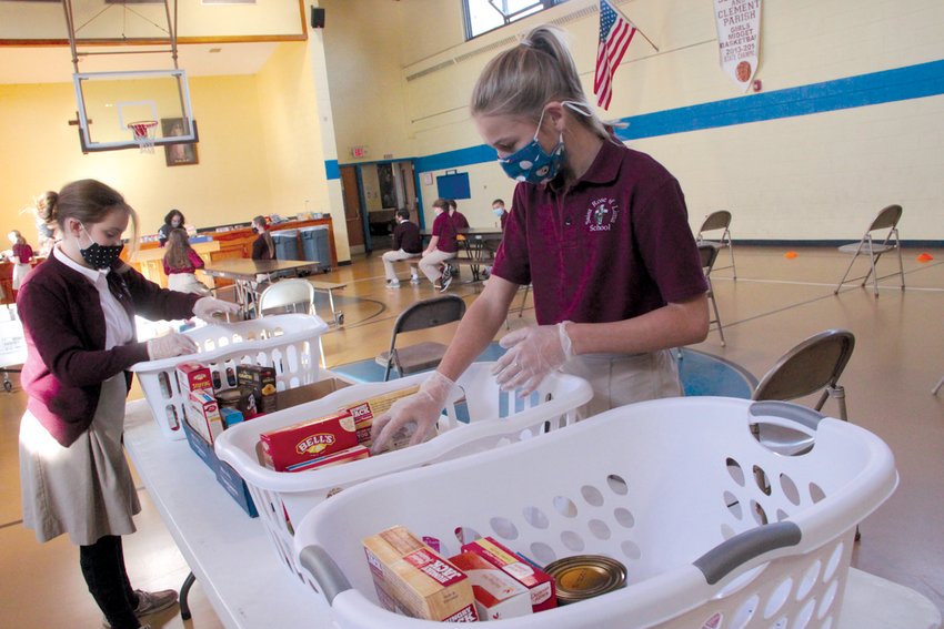 PACKING IT IN:&nbsp; Seventh graders Chloe Burns and Madelynn Iozzi pack one of 30 food baskets the school assembled for donation through Sts. Rose and Clement Church.