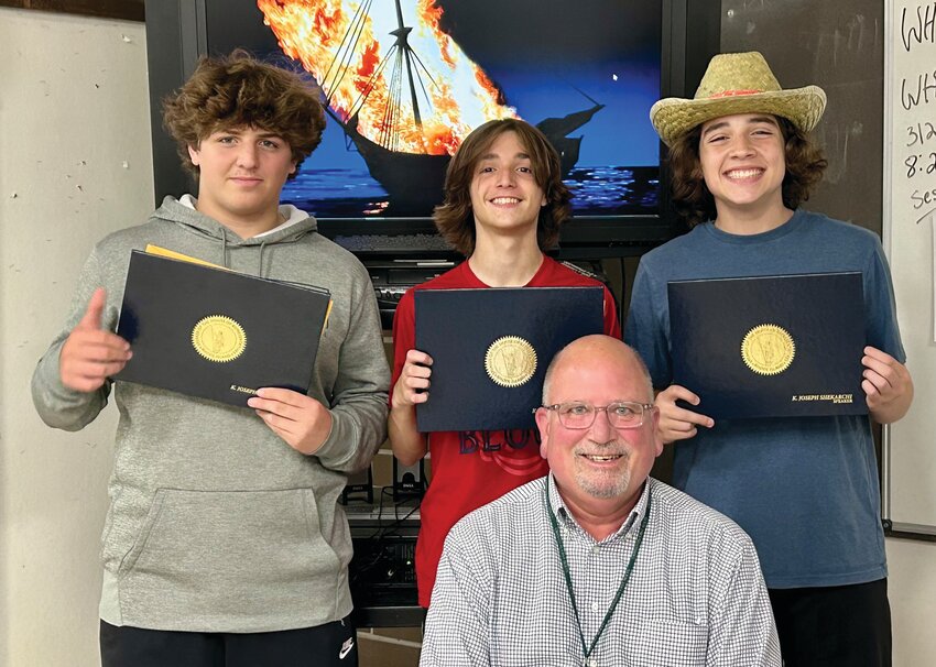 TOP THREE: Teacher Henry Maine sits in front of his three students, and essay contest winners, Giulio, Wesely, and Nathan (left to right) who swept the Gaspee Day essay writing contest with their essays about the Boston Massacre. (Submitted photo)