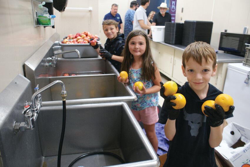 PREPPING THE FRUIT: Volunteers eight-year-old Logan Hopgood (left), seven-year-old Anastasia Champaga, and six-year-old Oliver Hopgood join forces to wash up the fruit offered at the barbeque. (Photos by Steve Popiel)