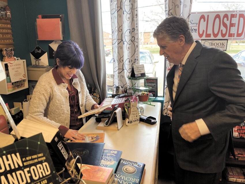 AT THE BOOK NOOK: McKee buys two books from Tracy Doyle at Mary&rsquo;s Paperbacks for his granddaughter. The governor mentioned that while it was too late for reading week, the Disney-themed Easter book was just in time for another holiday.