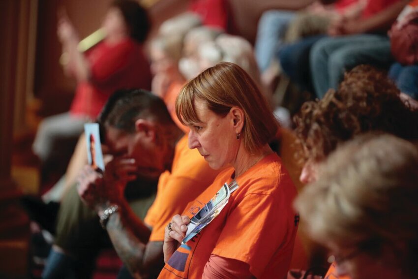 SAFER STORAGE: Claudia Townend of Charlestown holds a photo of Dillon Viens, 16, of Johnston, the victim of a fatal 2022 accidental shooting, in the west House Gallery during the House floor debate on a firearms safe storage bill on Tuesday, May 28, 2024. Dillon&rsquo;s father, David Viens, is shown in the background at left, holding up a photo of his son. (Alexander Castro/Rhode Island Current)