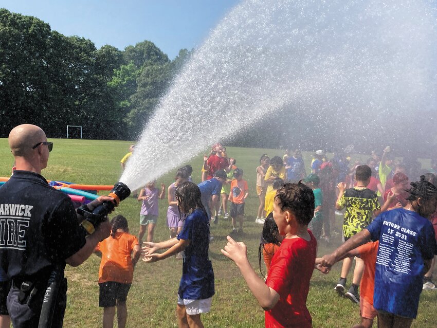 SOME EARLY HEAT RELIEF: An end of the school year field day was held last Friday at Lippitt School and to the delight of students Warwick firefighters were there to spray them down. Here firefighter Mark Kusal directs spray on willing students. Story and more photos on page 8. (Warwick Beacon photos by Adam Zangari)