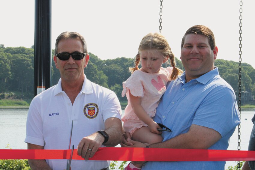 RIBBON CUTTING: Mayor Picozzi, joined by Councilman McAllister and his daughter, Grace McAllister, prepares to cut the ribbon to officially open the swing set. (Warwick Beacon photos)