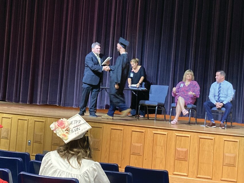 CROSSING THE STAGE: Graduate Joshua Czerwien shakes hands with Pilgrim principal Toby Gibbons as he hands him his diploma. In the foreground, Dorena Ayres&rsquo;s decorated graduation cap reads &ldquo;Better Late than Never.&rdquo;