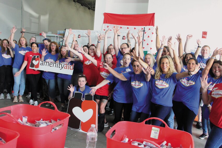 A CHEER FOR AMENITY: Blue Cross and Blue Shield employees take a break from assembling travel kits at Amenity Aid in Warwick for a group photo and to applaud the work of the nonprofit to end hygiene insecurity. (Cranston Herald photos)