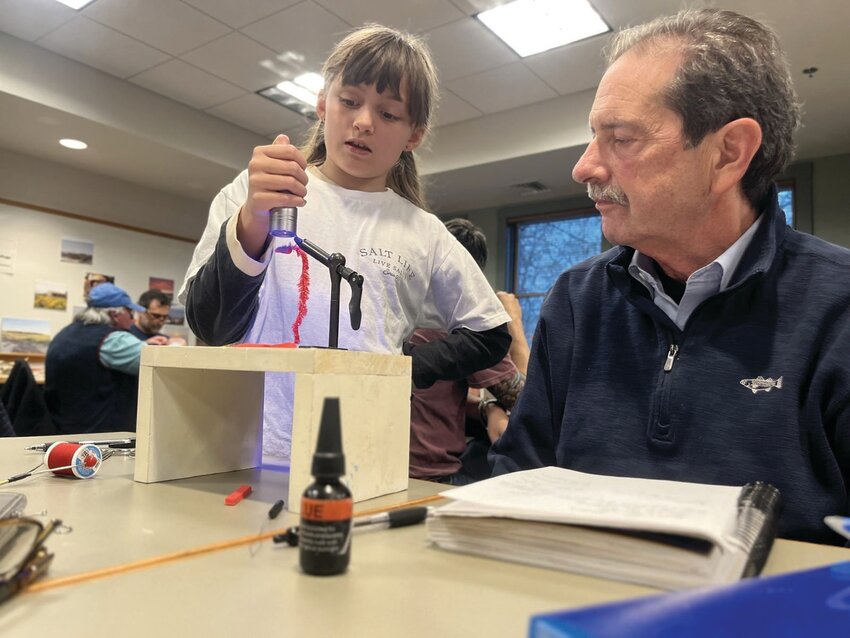 Rosie Clifton (eight), fly instructor, shows Capt. Dave Monti, student, how to dry glue on a fly with an ultraviolet light at the Cinder Worm Workshop. Submitted photo by Todd Corayer