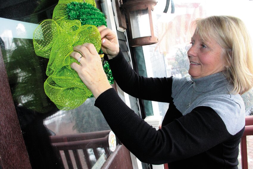 Laurie O&rsquo;Rourke affixes an Irish-themed wreath to O&rsquo;Rourke&rsquo;s Bar &amp; Grill in 2018 in celebration of St. Patrick&rsquo;s Day. Her work on Gaspee Days has earned her the first Benjamin Lindsay Award.