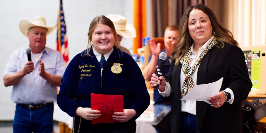 Sydney van Cleave holds a card representing the 34th hay bale auctioned off for the evening as emcee Jackie Rodieck prepares to make some remarks.