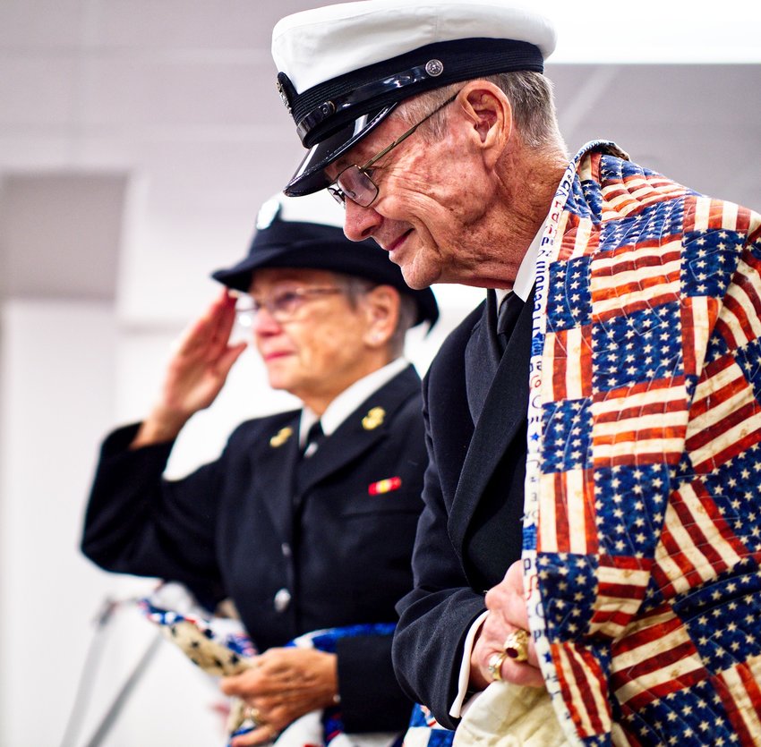 Barbara Melott salutes as Doc Melott grasps his newly-received quilt. The couple, both navy veterans of Vietnam, were touched and grateful for the gesture of support given to them Friday at the Quilts of Valor ceremony in Quitman.